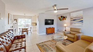 A living room with a sofa, armchair, TV, ceiling fan, and artwork on the wall. - Dog-Friendly, Snowbird-Ready Florida Escape – Near Beaches & Golf (Port Charlotte)