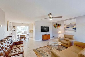Ein Wohnzimmer mit Sofa, Sessel, Fernseher, Deckenventilator und Bildern an der Wand.