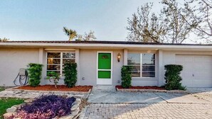 A single-story house with a garage, a green door, and a small front yard with shrubs and a stone pathway. - Dog-Friendly, Snowbird-Ready Florida Escape – Near Beaches & Golf (Port Charlotte)