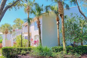 A building with a white exterior, a staircase leading to a balcony, and palm trees in the foreground. - 2nd-floor lakefront condo with heated pool, lake view, balcony, bikes, fast WiFi (Naples)