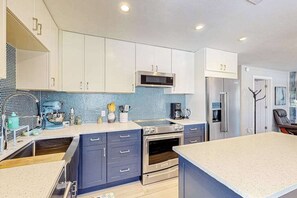 A modern kitchen with white cabinets, a blue backsplash, stainless steel appliances, and a large island.