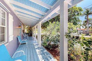 A covered porch with seating, a garden, and a view of the surrounding area.