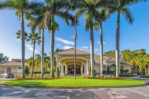A building with a central entrance, palm trees, and a flagpole. - Resort community home with bikes, screened porch, on-site golf, & AC (Naples)