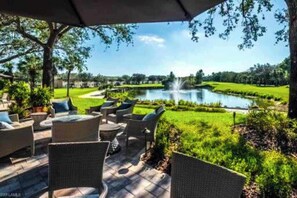 Eine Terrasse im Freien mit Korbmöbeln, Blick auf einen Teich und einen Golfplatz im Hintergrund.