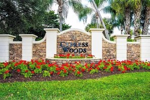 A sign for Cypress Woods with a stone wall and red flowers in front. - Resort community home with bikes, screened porch, on-site golf, & AC (Naples)