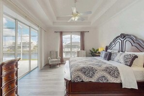 Ein Schlafzimmer mit einem großen Bett, einem Deckenventilator, einem Fenster mit Vorhängen und Blick auf Gebäude.
