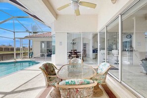 Ein Poolbereich mit Korbstühlen, einem Glastisch und einem Deckenventilator.