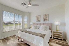 A bedroom with a bed, two bedside tables, a ceiling fan, and a window with blinds. - Newly Remodeled Chic Condo on the GreenLinks golf course with lanai, pool. (Naples)