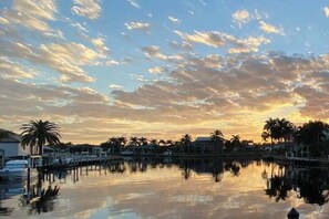 Blick auf das Wasser mit ruhiger Wasseroberfläche, die Himmel, Palmen und Gebäude am Ufer reflektiert.