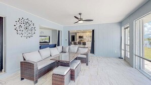 Un salon moderne avec une table basse en verre, un canapé en osier et un ventilateur de plafond.