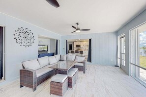 A modern living room with a glass coffee table, wicker sofa, and a ceiling fan. - Stylish Waterfront Escape | Sunroom Views, Full Renovation, A/C & Prime Location (Port Charlotte)