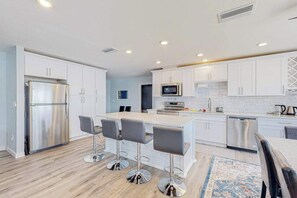 A modern kitchen with white cabinets, stainless steel appliances, and a central island with bar stools. - Stylish Waterfront Escape | Sunroom Views, Full Renovation, A/C & Prime Location (Port Charlotte)