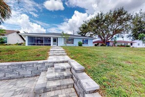 A residential house with a stone staircase leading to the front door, a large tree, and a clear sky. - Stylish Waterfront Escape | Sunroom Views, Full Renovation, A/C & Prime Location (Port Charlotte)