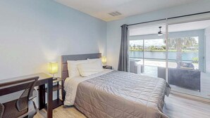 Une chambre d’hôtel équipée d’un lit, d’un bureau, d’une chaise et d’une grande porte-fenêtre coulissante donnant sur un espace extérieur.