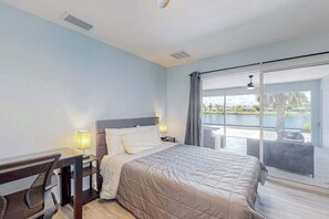 A hotel room with a bed, desk, chair, and a large sliding glass door leading to an outdoor area. - Stylish Waterfront Escape | Sunroom Views, Full Renovation, A/C & Prime Location (Port Charlotte)