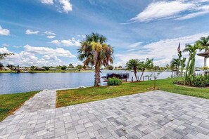 A paved patio area with a view of a lake and palm trees. - Stylish Waterfront Escape | Sunroom Views, Full Renovation, A/C & Prime Location (Port Charlotte)