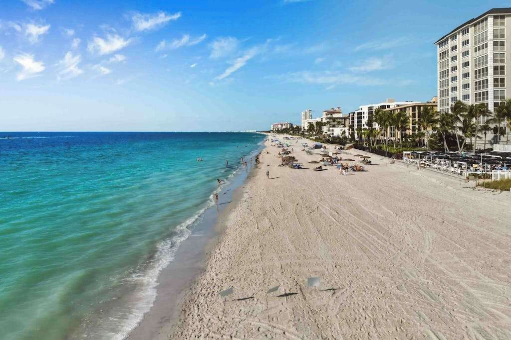 A beach with a hotel on the right, clear blue water, and a sandy shore.