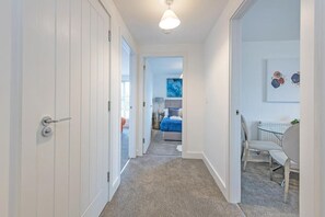 A hallway leading to a bedroom with a bed, a desk, and a chair.