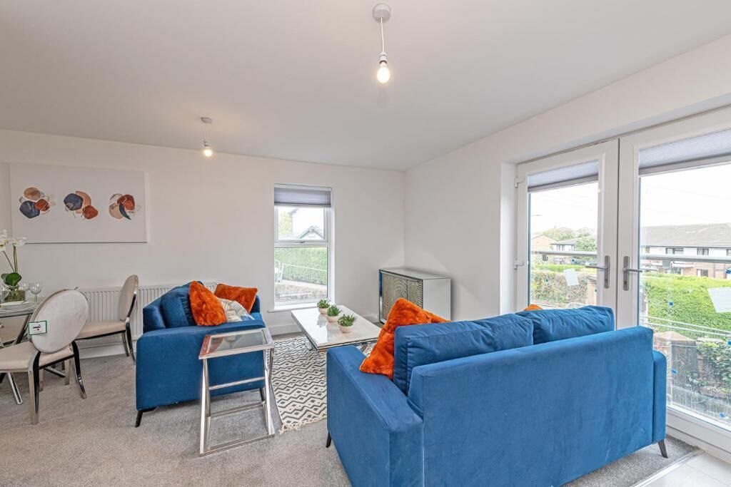 Een moderne woonkamer met een blauwe bank, een bijzettafeltje en een eethoek met een witte tafel en stoelen.