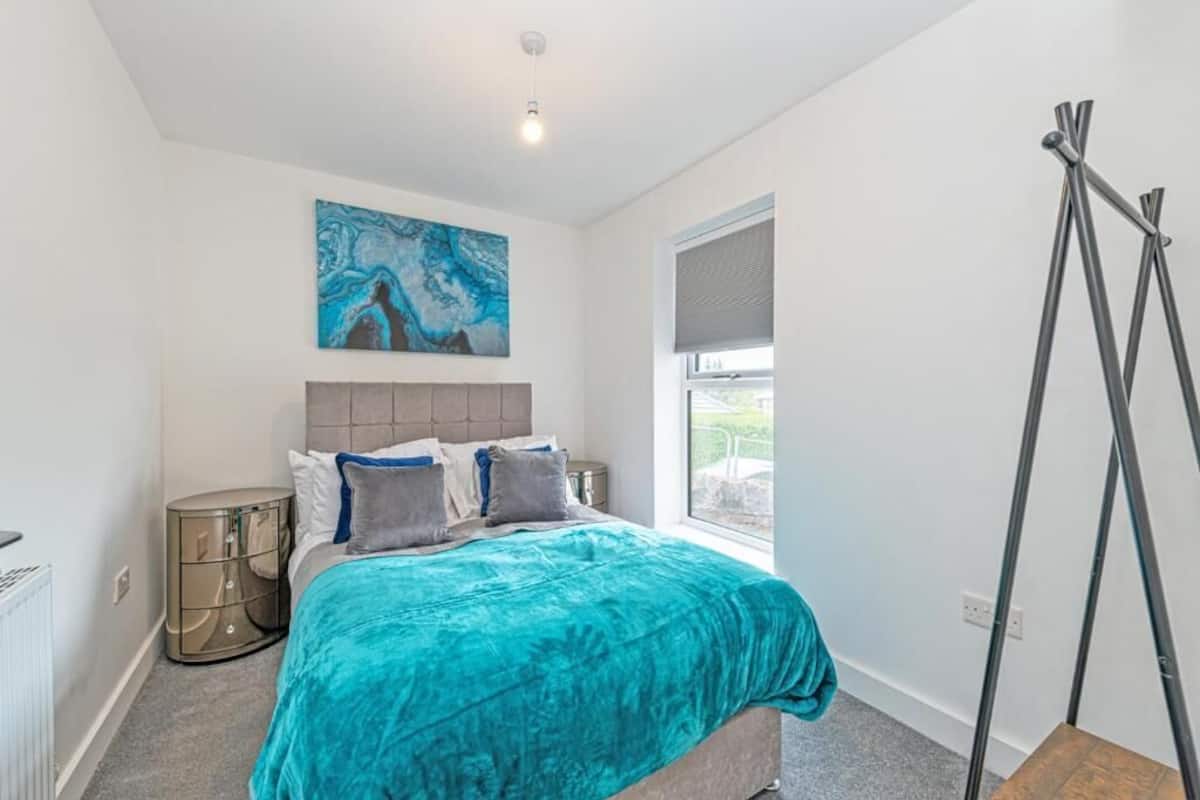A bedroom with a bed, a painting, a window, and a radiator.