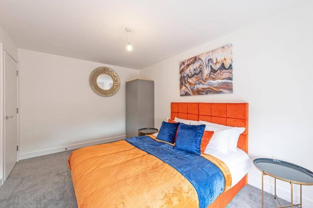 A bedroom with a bed, a round mirror, a grey wardrobe, a small round table, and a painting on the wall.