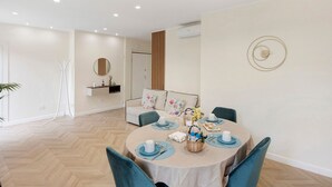 Een eetruimte met een ronde tafel voor vier personen, omringd door stoelen, met een bank en een wandplank op de achtergrond.