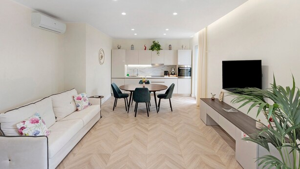 Een moderne woonkamer met een bank, een eettafel, stoelen, een televisie en een keuken op de achtergrond.
