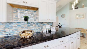 A kitchen with white cabinets, a black granite countertop, and a blue and white mosaic backsplash. - Canal-Front w/Private Pool & Dock – Your Florida Escape Starts Here (Punta Gorda)