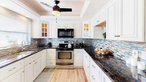A modern kitchen with white cabinets, a black countertop, and a backsplash with blue and white tiles. - Canal-Front w/Private Pool & Dock – Your Florida Escape Starts Here (Punta Gorda)