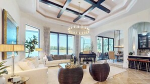 A spacious living room with a piano, large windows, and a dining area. - Deluxe home in a resort community with amazing views, pool, & hot tub (Naples)