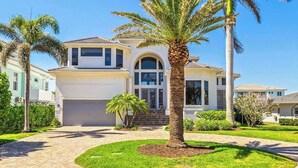 A two-story house with a garage, a driveway, and a well-maintained lawn with palm trees. - Exquisite waterfront home with lanai, heated pool and spa(hot tub), and internet (Naples)