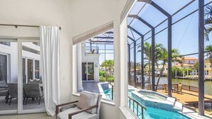 A room with a bed, a chair, a large window with a view of a pool and a building. - Exquisite waterfront home with lanai, heated pool and spa(hot tub), and internet (Naples)
