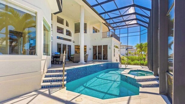 A modern house with a glass-enclosed patio, a swimming pool, and a two-story structure. - Exquisite waterfront home with lanai, heated pool and spa(hot tub), and internet (Naples)