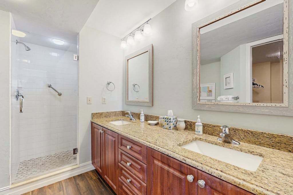 A bathroom with a shower, two sinks, a large mirror, and wooden cabinets.