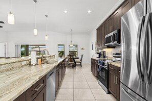 A modern kitchen with a central island, stainless steel appliances, and pendant lighting. - Dog-Friendly Waterfront Escape with Heated Pool & Outdoor Grill (Cape Coral)