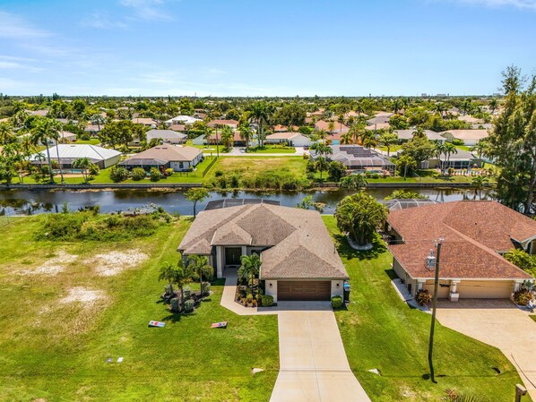 A residential area with houses, a body of water, and a well-maintained lawn. - Dog-Friendly Waterfront Escape with Heated Pool & Outdoor Grill (Cape Coral)