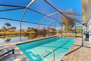 A swimming pool with a clear view of the surrounding landscape, a covered patio area, and a poolside lounge chair. - Spacious coastal home, dog-friendly, private heated pool & close to everything (Cape Coral)