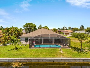 A residential property with a swimming pool, a covered patio, and a lawn. - Dog-Friendly Waterfront Escape with Heated Pool & Outdoor Grill (Cape Coral)