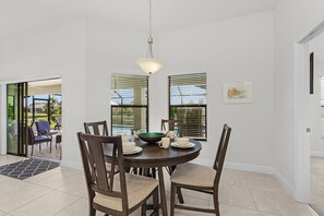 A dining area with a round table, chairs, and a hanging light fixture. - Dog-Friendly Waterfront Escape with Heated Pool & Outdoor Grill (Cape Coral)