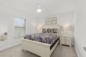 Ein Schlafzimmer mit Bett, Nachttischen, Deckenventilator, Fenster mit Jalousien und einem Wandbild.