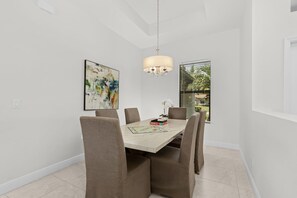 Un comedor con una mesa de mármol, sillas acolchadas, una araña y un cuadro abstracto grande en la pared.