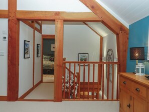A room with a wooden staircase, a bed, a desk with a lamp, and framed pictures on the wall. - Pylemoor Cottage (Tiverton)