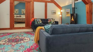 A cozy loft bedroom with a sloped ceiling, a built-in wood-burning stove, a blue sofa, and a patterned rug. - Pylemoor Cottage (Tiverton)