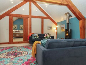 Ein gemütliches Schlafzimmer im Loft-Stil mit schrägem Dach, einem eingebauten Kaminofen, einem blauen Sofa und einem gemusterten Teppich.