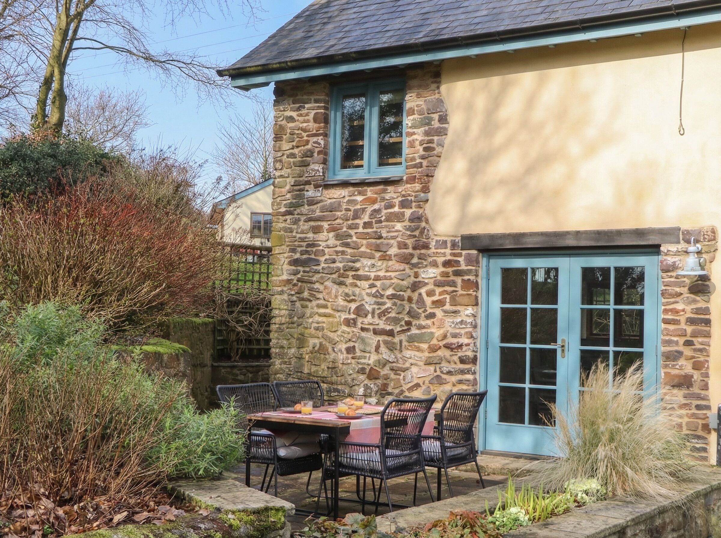 A stone building with a blue door and window, a table with chairs, and a garden area.