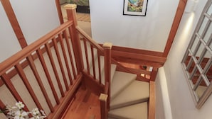 A wooden staircase with a handrail, beige carpeted steps, and a small wooden stool. - Pylemoor Cottage (Tiverton)
