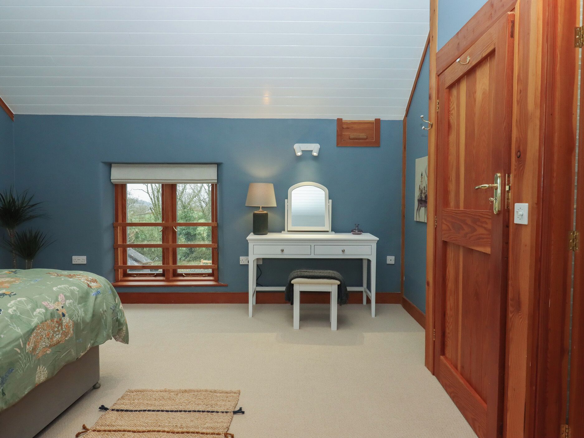 A bedroom with a bed, a desk, a chair, a window, and a door.