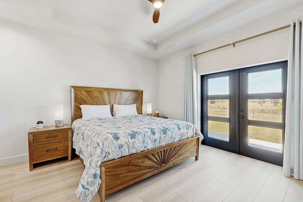 A bedroom with a wooden bed, a nightstand, a window with curtains, and a ceiling fan.