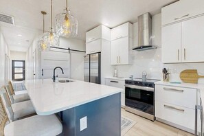 A modern kitchen with white cabinets, a central island, stainless steel appliances, and pendant lighting. - Placida at Meadows & Villas; brand-new duplex, dogs OK, golf courses nearby (Placida)