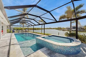 A swimming pool with a mosaic edge, a covered patio area, and a view of a lake. - Spacious canal front home with private pool, dock & close to everything (Marco Island)